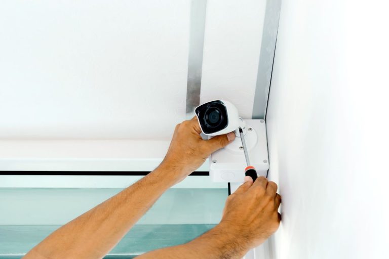 A man adjusts a camera mounted on a wall, focusing on securing it in place.