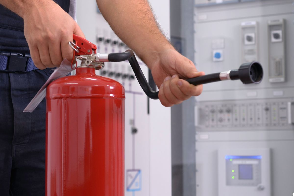 A man in a blue shirt stands holding a fire extinguisher, ready to respond to a fire emergency.