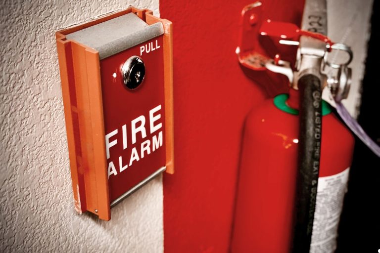 Fire alarm system mounted on a wall in a commercial building, featuring a red alarm box and emergency exit signage.
