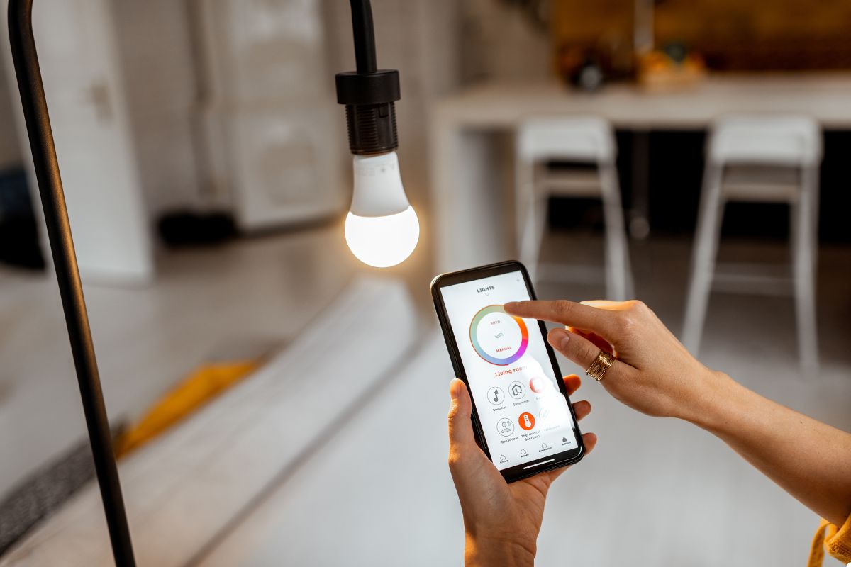 A person operates a smartphone to adjust the brightness of a smart light bulb in a modern setting.