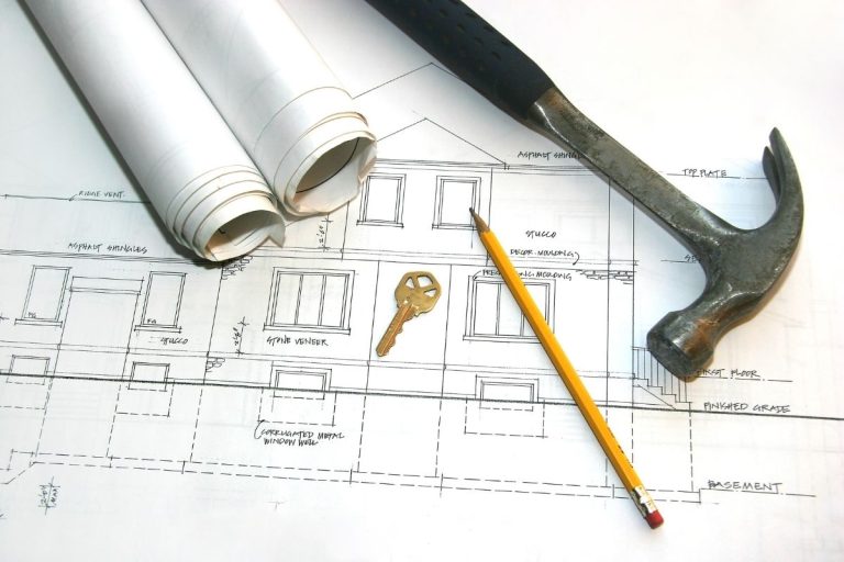 A hammer, pencil, and blueprint are arranged on a wooden table, suggesting a construction or design project in progress.